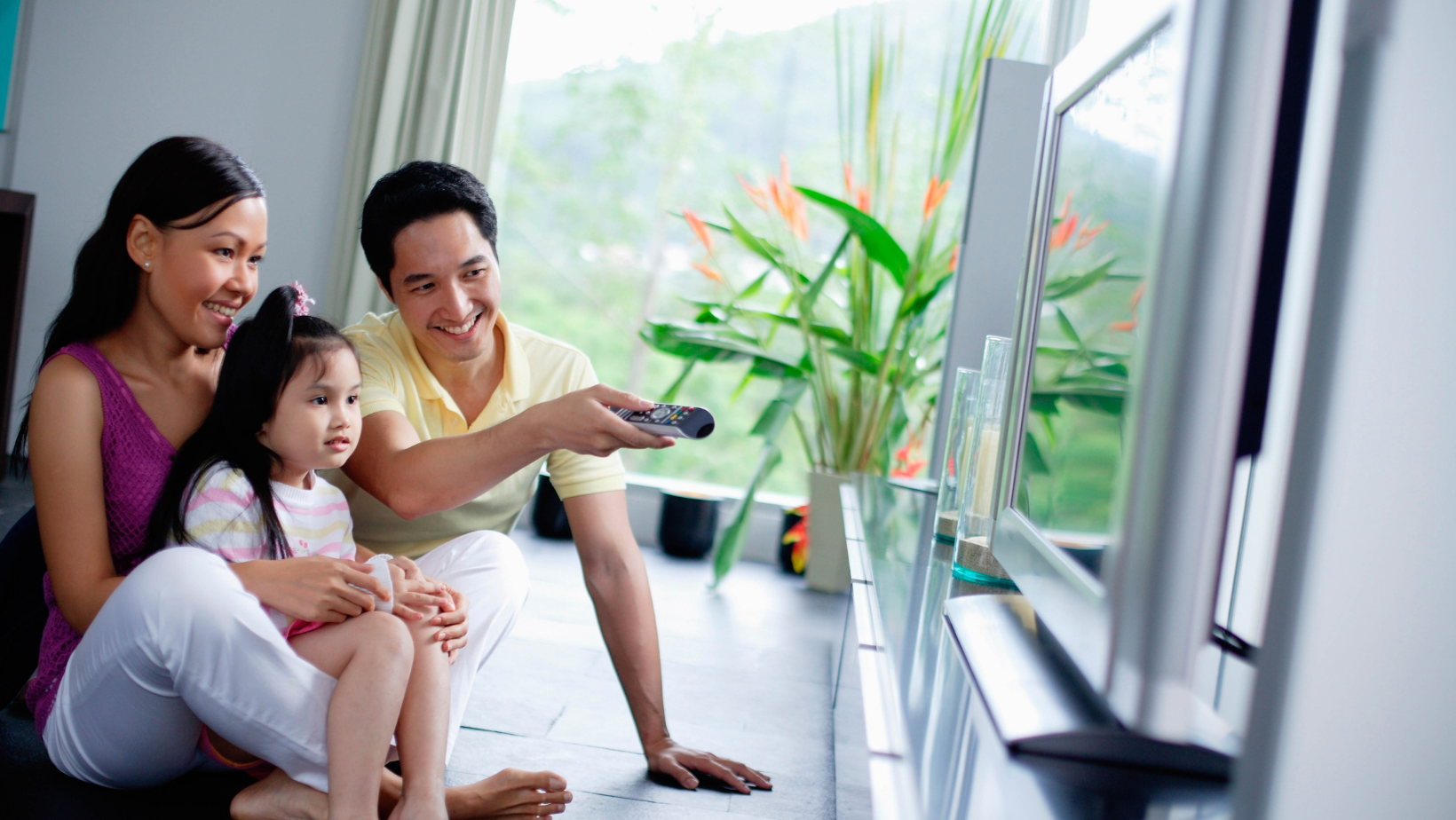 two parents and child looking at tv - one parent holding remote