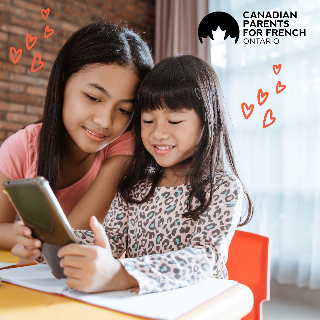 two young girls age 5-12 smiling at a tablet with hearts floating beside them